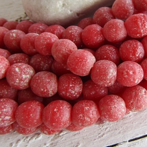 Puede incluir: Una hebra de cuentas de vidrio rojas con una superficie texturizada y moteada.