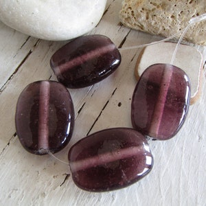 May include: Four purple glass beads with a white stripe down the centre. The beads are strung on a clear thread.