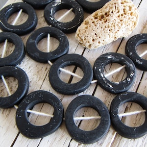 Op de afbeelding: Een streng zwarte, ronde houten kralen met een wit touwtje geregen door de middelste gaten. De kralen zijn licht onregelmatig van vorm en hebben een matte afwerking.