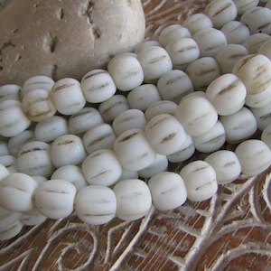 Op de afbeelding: Een streng witte glazen kralen met bruine strepen. De kralen zijn rond en hebben een licht onregelmatige vorm.