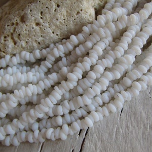 May include: A strand of white, opaque, glass beads. The beads are small and have a slightly irregular shape. They are arranged in a loose, flowing pattern.