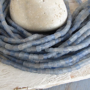 Può includere: Un filo di perline di vetro blu chiaro, con finitura opaca, disposte a spirale su una superficie di legno.