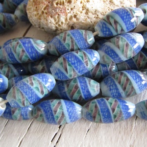 May include: A strand of blue, green, and white glass beads with a swirling pattern. The beads are oval shaped and have a glossy finish.