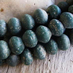 Könnte beinhalten: Eine Schnur dunkelgrüner, gesprenkelter Perlen. Die Perlen sind rund und haben eine raue, strukturierte Oberfläche.