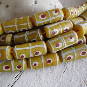Può includere: Primo piano di una collana di perline di vetro giallo con disegni dipinti in bianco e rosso. Le perline sono cilindriche e hanno una finitura lucida.