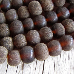 以下が含まれることがあります： ざらざらとした質感の暗い茶色の琥珀のビーズのネックレス。ビーズは丸く、わずかにオレンジがかった色合いをしています。