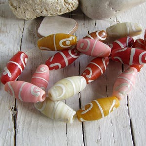 Può includere: Una collezione di perline ovali colorate con motivi a spirale bianchi. Le perline sono in vetro e hanno una finitura lucida.