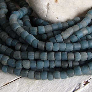 May include: A close-up of a strand of blue glass beads. The beads are small and round, and they have a matte finish.