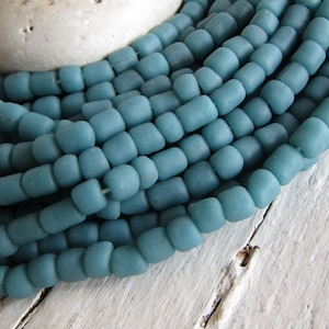 Op de afbeelding: Een streng tealblauwe glazen kralen. De kralen zijn rond en hebben een matte afwerking.