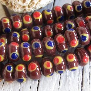 Può includere: Una collana di perline di vetro marrone con pois gialli, rossi e blu. Le perline sono di forma ovale e hanno una finitura lucida.