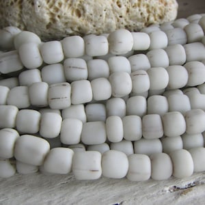 Puede incluir: Una hebra de cuentas de vidrio blanco con un acabado ligeramente esmerilado. Las cuentas son redondas y tienen una textura sutil e irregular.