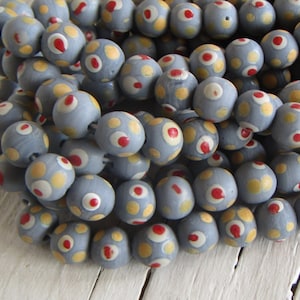 Pode incluir: Um fio de contas de madeira cinzas com bolinhas brancas e vermelhas. As contas são redondas e têm um acabamento fosco.