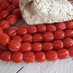 May include: A strand of bright orange glass beads with a ribbed texture. The beads are round and have a slightly oval shape.