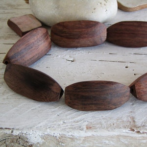 Può includere: Un primo piano di una collana di perline di legno di colore marrone scuro. Le perline sono di forma ovale e hanno una finitura liscia e lucida.