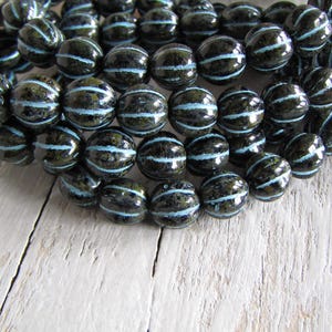 Könnte beinhalten: Eine Strähne aus schwarzen und blauen Glasperlen mit einem gestreiften Muster. Die Perlen sind rund und haben eine glänzende Oberfläche.