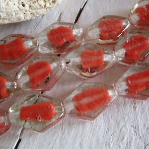 May include: A strand of clear glass beads with red, opaque, irregular shapes inside. The beads are faceted and have a diamond-like shape.