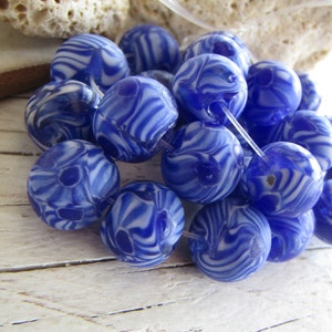 May include: A collection of blue and white glass beads with a swirling pattern. The beads are round and have a glossy finish.