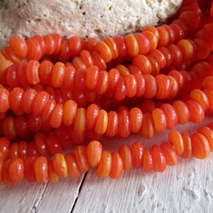 Può includere: Una collana di perline di vetro a strisce arancioni e gialle. Le perline sono rotonde e hanno una forma leggermente irregolare. Sono infilate su un filo trasparente.