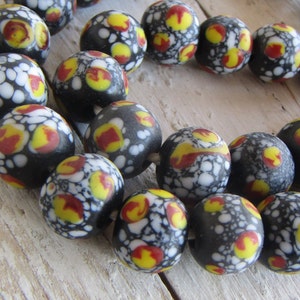 Può includere: Una collana di perline di vetro nero con macchie bianche e gialle e accenti rossi.