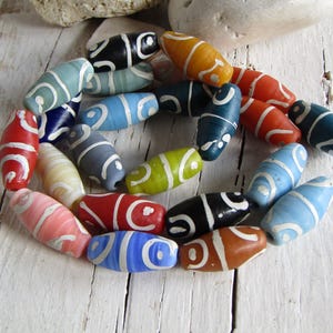 Può includere: Una collezione di perline di vetro colorate con vortici bianchi. Le perline sono di forma ovale e hanno una finitura lucida.