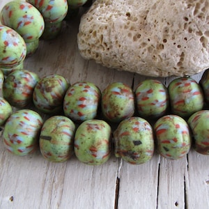 以下が含まれることがあります： 赤と青の渦巻き模様が入った緑色のガラスビーズのネックレス。ビーズは丸く、まだら模様になっています。