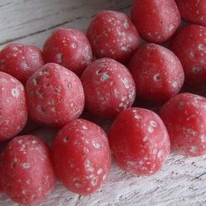 May include: A strand of coral beads, each bead is a deep red color with a speckled white texture.