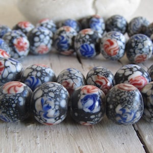 Può includere: Una collana di perline in ceramica nera, bianca, blu e rossa con un motivo floreale. Le perline sono rotonde e hanno una superficie testurizzata.