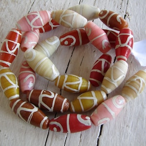 Può includere: Una collana di perline ovali in vari colori, tra cui rosso, rosa, giallo e marrone. Ogni perlina presenta un disegno bianco a spirale. Le perline sono infilate insieme, creando una forma circolare.