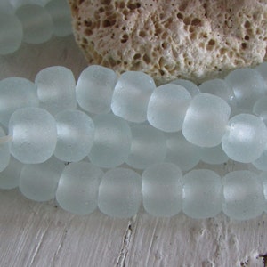 Könnte beinhalten: Eine Strähne aus gefrosteten Glasperlen in hellblauer Farbe. Die Perlen sind rund und haben eine leicht unregelmäßige Form.