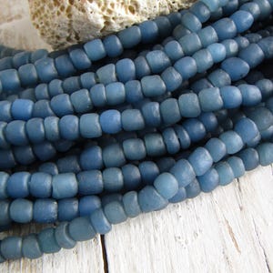 Op de afbeelding: Een streng blauwe glazen kralen, elke kraal is licht onregelmatig van vorm en heeft een matte afwerking.