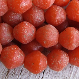 Puede incluir: Una hebra de cuentas de vidrio naranja con un acabado texturizado y esmerilado. Las cuentas son hexagonales y tienen un aspecto ligeramente irregular, hecho a mano.