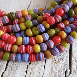 May include: Strands of colorful, striped beads in red, blue, green, yellow, and brown. The beads are strung together, creating a textured and vibrant display. The beads are likely made of glass or a similar material.