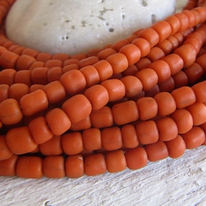 Può includere: Primo piano di una collana di perline arancioni. Le perline sono rotonde e hanno una finitura opaca. Sono disposte in un motivo circolare.