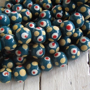 Può includere: Perle rotonde di colore blu-verde con pois bianchi e rossi. Le perle sono in legno e hanno una finitura lucida.