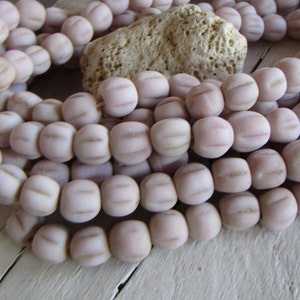 Könnte beinhalten: Eine Strähne aus hellrosa Glasperlen mit einer strukturierten Oberfläche. Die Perlen sind rund und haben eine leicht ovale Form.