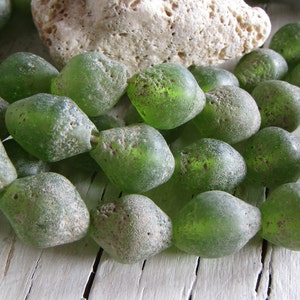 Könnte beinhalten: Eine Kette aus grünen Glasperlen mit einer rauen, strukturierten Oberfläche. Die Perlen sind unregelmäßig geformt und haben eine leicht durchscheinende Optik.