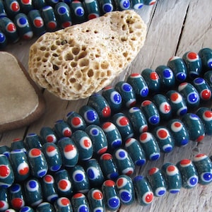 May include: A strand of teal blue glass beads with white and red polka dots. The beads are oval shaped and have a glossy finish.
