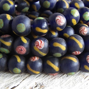 Può includere: Una collana di perline di vetro blu scuro con motivi colorati. Le perline hanno accenti gialli, bianchi, rossi e verdi.