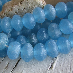 Könnte beinhalten: Eine Strähne aus hellblauen Glasperlen mit mattem Finish. Die Perlen sind rund und haben eine leicht unregelmäßige Form.