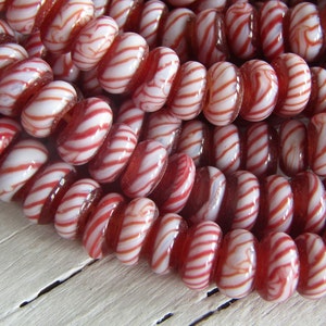 Può includere: Una collana di perline di vetro rosse e bianche con un motivo a spirale di bastoncino di zucchero. Le perline sono rotonde e hanno una finitura lucida.