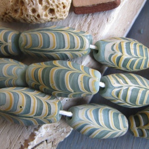 May include: A strand of oval-shaped glass beads with a marbled pattern of blue, green, and yellow. The beads are strung on a white cord.