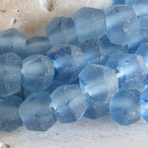 Könnte beinhalten: Eine Strähne aus hellblauen Glasperlen mit einer facettierten, unregelmäßigen Form. Die Perlen haben eine matte, durchscheinende Oberfläche.