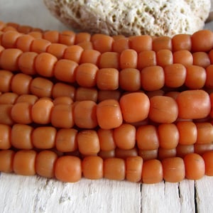 May include: A strand of orange glass beads. The beads are round and have a matte finish. They are strung on a clear thread.