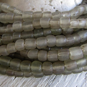 May include: A strand of gray glass beads with a slightly frosted finish. The beads are round and have a slightly irregular shape. The beads are strung on a clear thread.