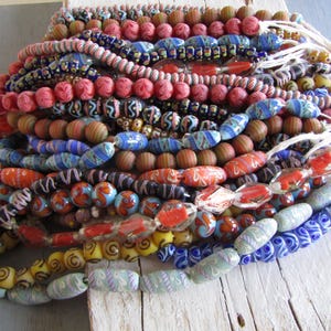 Può includere: Una collezione di perline di vetro colorate di varie forme e dimensioni. Le perline sono infilate insieme, con sfumature di rosso, blu, giallo e marrone. Alcune perline hanno motivi intricati, mentre altre sono di colori solidi. Le perline sono probabilmente per la creazione di gioielli.