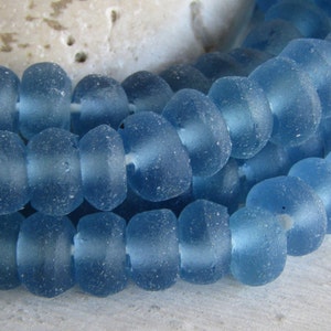 May include: A strand of light blue glass beads with a frosted finish. The beads are round and have a slightly irregular shape.