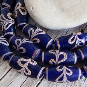 Könnte beinhalten: Eine Reihe dunkelblauer Glasperlen mit weißen und roten Wirbelmustern. Die Perlen sind oval geformt und haben eine glänzende Oberfläche.