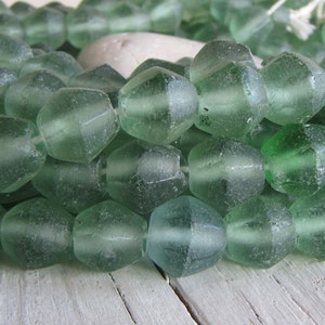 May include: A strand of green glass beads with a faceted, irregular shape. The beads are translucent and have a slightly frosted appearance.