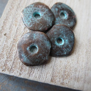 Op de afbeelding: Vier koperkleurige metalen kralen met een turquoise patina. Elke kraal heeft een rond gat in het midden.