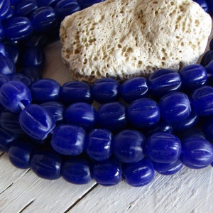 Può includere: Una collana di perline di vetro blu scuro con una texture a coste. Le perline sono di forma ovale e hanno una finitura lucida.